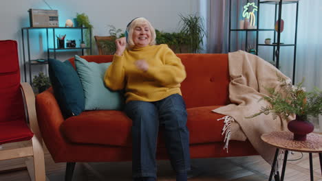 Happy-grandmother-old-woman-in-wireless-headphones-relaxing-on-sofa-at-home-listening-favorite-music