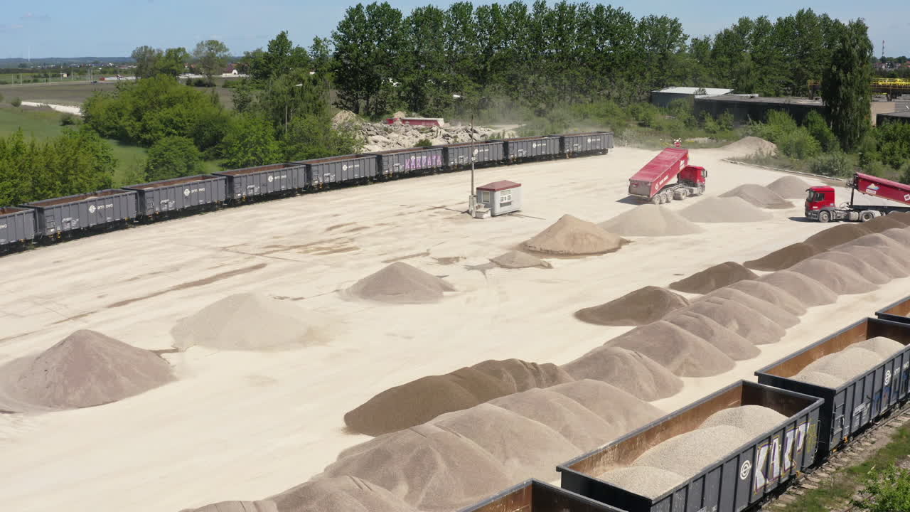 Dump Trucks And Loaded Freight Trains With Piles Of Sand At Industrial Site. descending drone shot