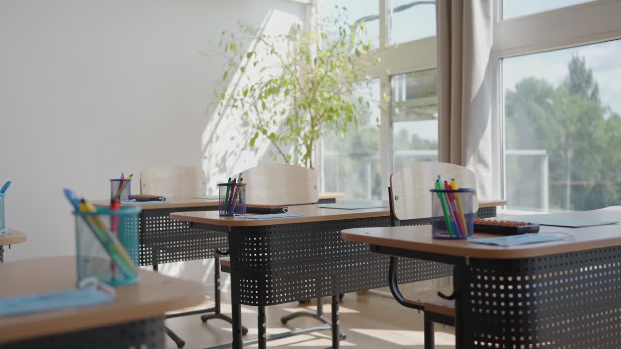 Rays of light falling to the empty dark classroom. The camera panning behind rows of desks and chairs. Teaching class without students during a break. Abandoned school. Disturbing mood.
