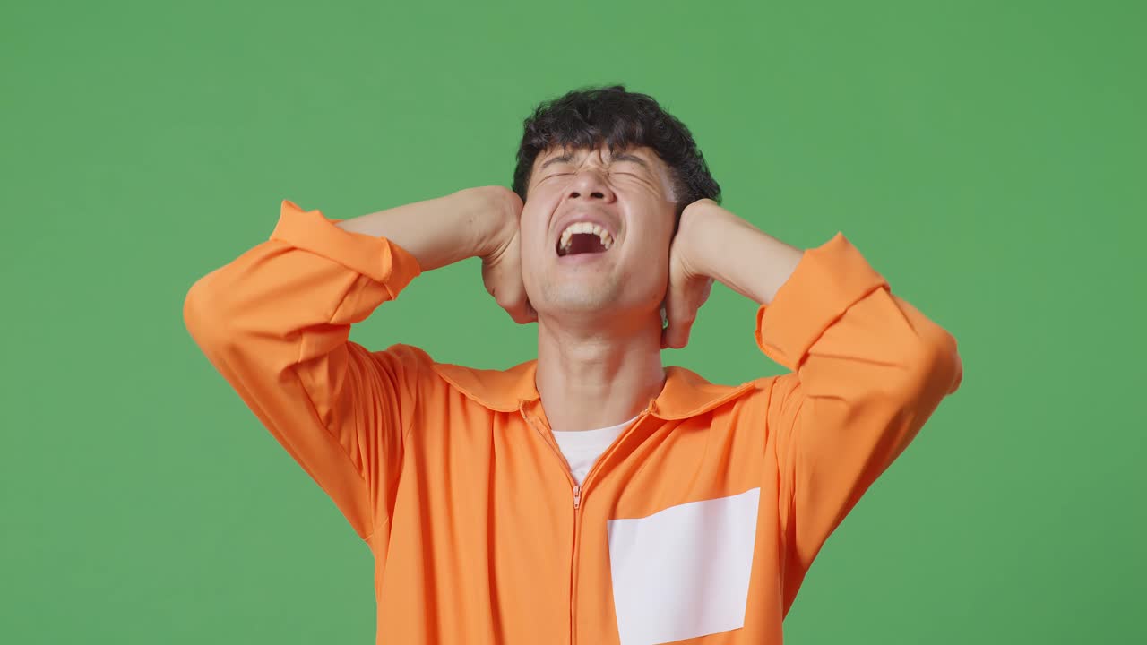 녹색 스크린 배경에 서서 큰 소리로 비명을 지르는 스트레스를 받은 아시아 남성 죄수