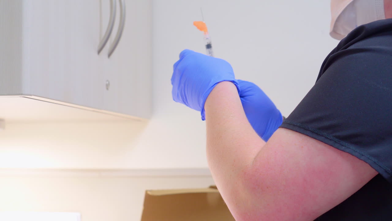 la enfermera prepara la vacuna covid 19 o la inyección de la vacuna contra el virus de la corona en un seringe mientras usa guantes y una máscara en el consultorio médico sin rostros