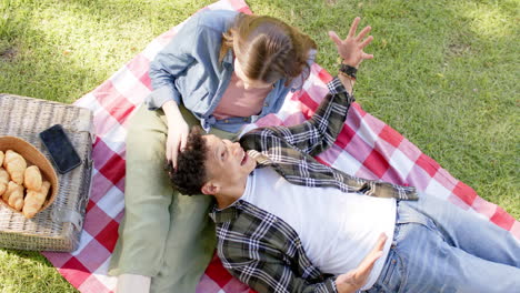 una pareja feliz y diversa tiene un picnic en un jardín soleado, en cámara lenta.