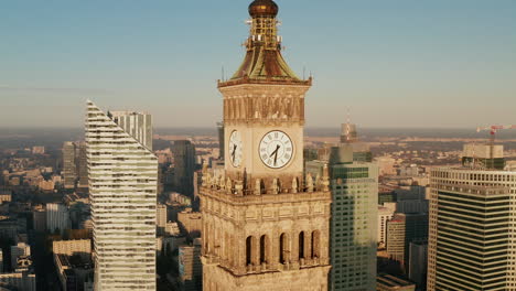 Pull-back-footage-of-tower-clock-on-top-of-high-rise--historic-building-in-soviet-style.-Modern-downtown-skyscrapers--in-background.-Warsaw,-Poland