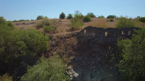 Abandoned-basalt-houses-and-a-jewish-village-in-the-area-of-Ein-Peak,-its-a-spring-in-the-south-of-the-golan-heights-and-a-remains-of-a-syrian-village,-kibbutz-afik-in-the-background