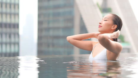 close-up of a sexy woman in a rooftop resort swimming pool pushing wet hair away from her face