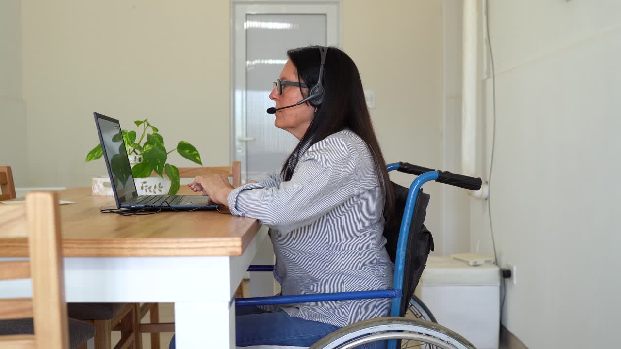 Woman In Wheelchair Put on Her Headphones And Starts Her Work With Laptop At Home. - wide shot