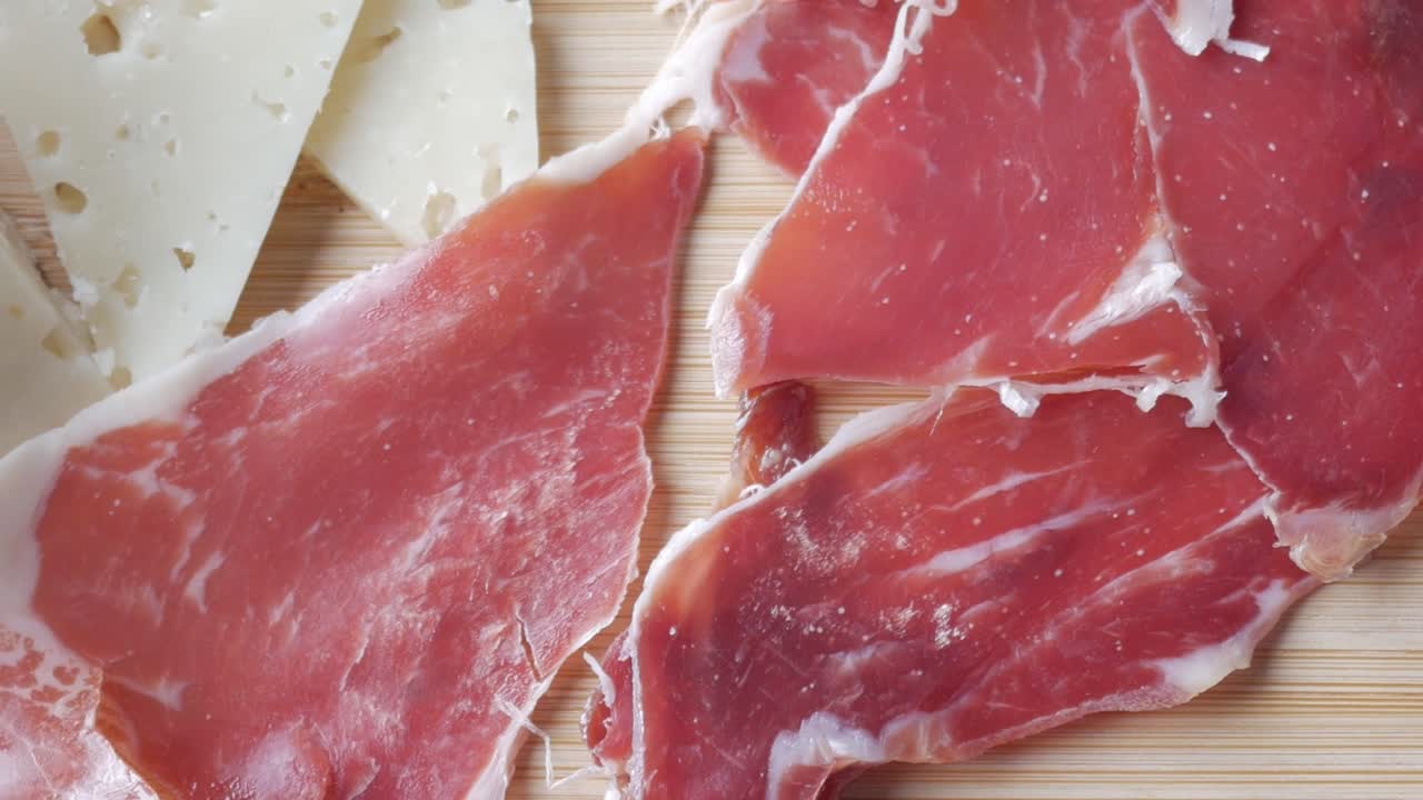 Thinly sliced ham and cheese on wooden board, appetizing food presentation