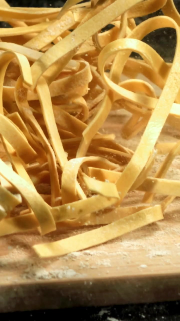 Tagliatelle fresche che cadono al rallentatore su un tagliere infarinato