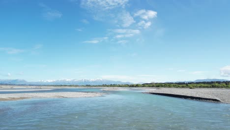 flying low upstream over braided waimakariri river in new zealand - beautiful turquoise water, blue sky and mountains on low horizon