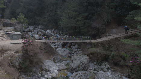 aerial view of tourists with local guides crossing bridge in nepal’s everest region, surrounded by serene hills and adventure trail under himalayan sky