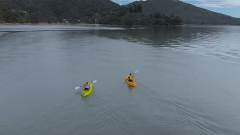 Two-people-kayaking-with-yachts-in-background-in-Marlborough-Sounds,-New-Zealand---Aerial