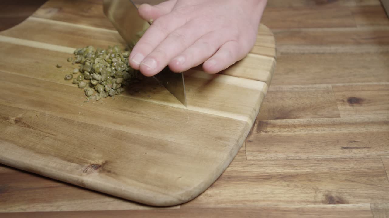 Chef che trita finemente, con coltello mannaia da cucina, capperi per preparare burro al caffè di Parigi, salsa perfetta per carni