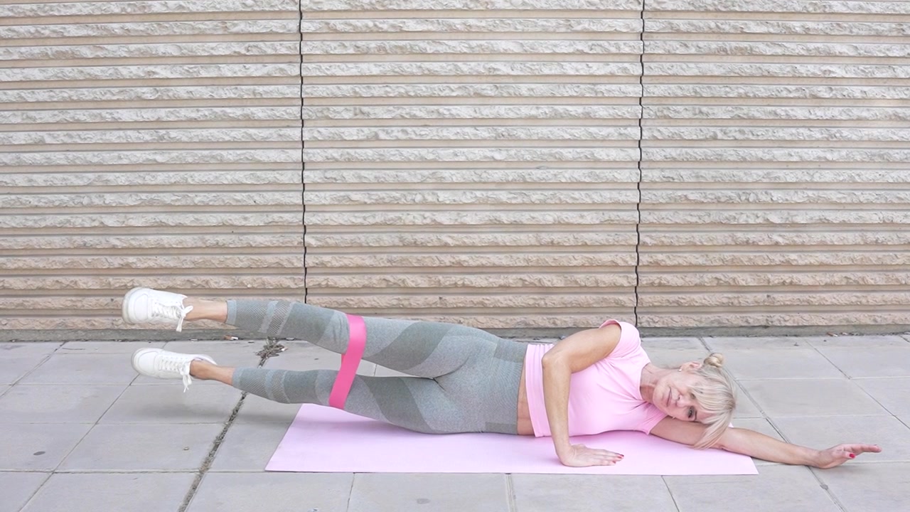 Una donna esegue sollevamenti laterali delle gambe con una fascia di resistenza all'aperto, concentrandosi su fitness e flessibilità.