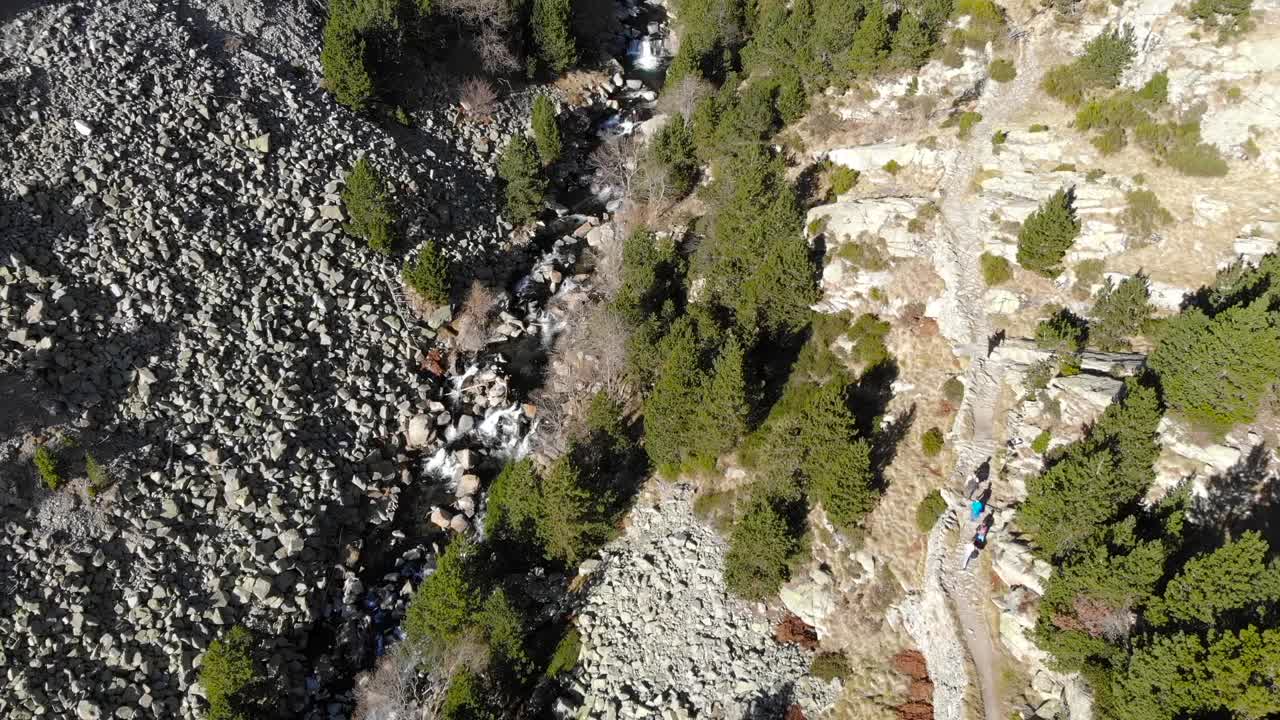 antena: toma cenital de un río y un grupo de excursionistas caminando por un sendero en las montañas en otoño
