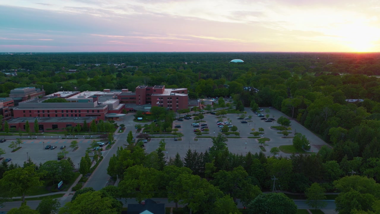 Volo con drone ad alta angolazione sopra un grande ospedale in mattoni e campus medico circondato da una fitta foresta di alberi durante il crepuscolo a Highland Park, Illinois.