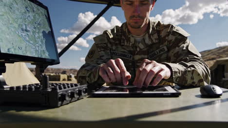 Military personnel using technology and maps in a field setting.