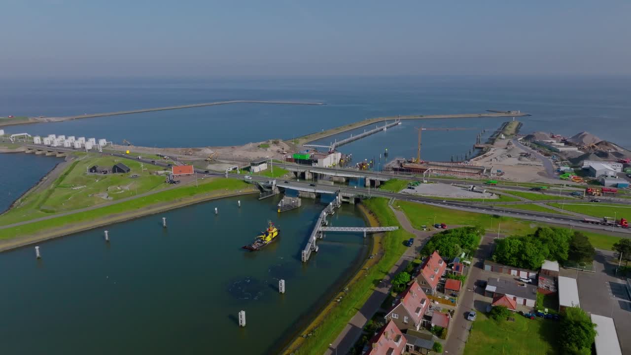 Drone semi orbit revealing the Afsluitdijk water locks, bridge network and nearby coastal village under clear daylight