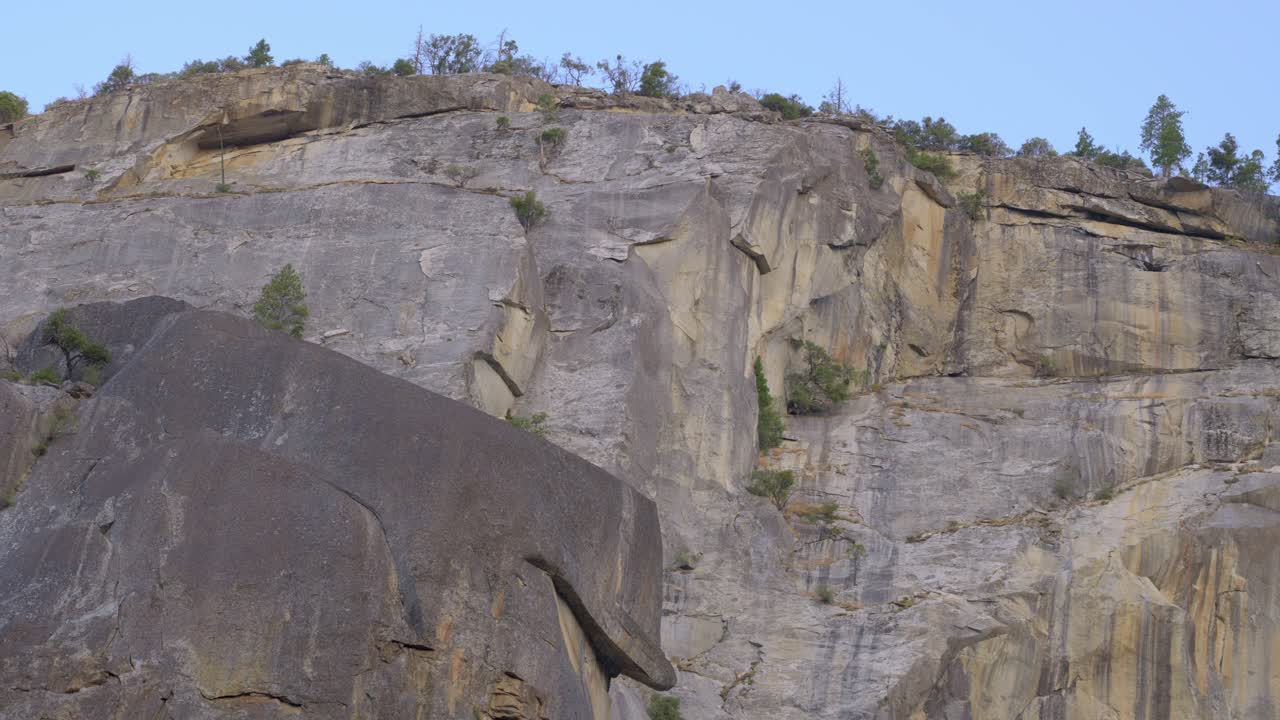 4K telephoto footage pans left to right along a massive Yosemite granite mountainside, revealing crags, ledges, and weather-etched textures in crisp detail. Ideal for nature and geology projects
