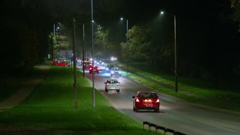a nighttime scene of a road lined with glowing street lights as cars travel in both directions, creating a lively urban atmosphere