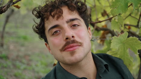 man posing grape plantation at vine bush vertically closeup. happy guy smiling