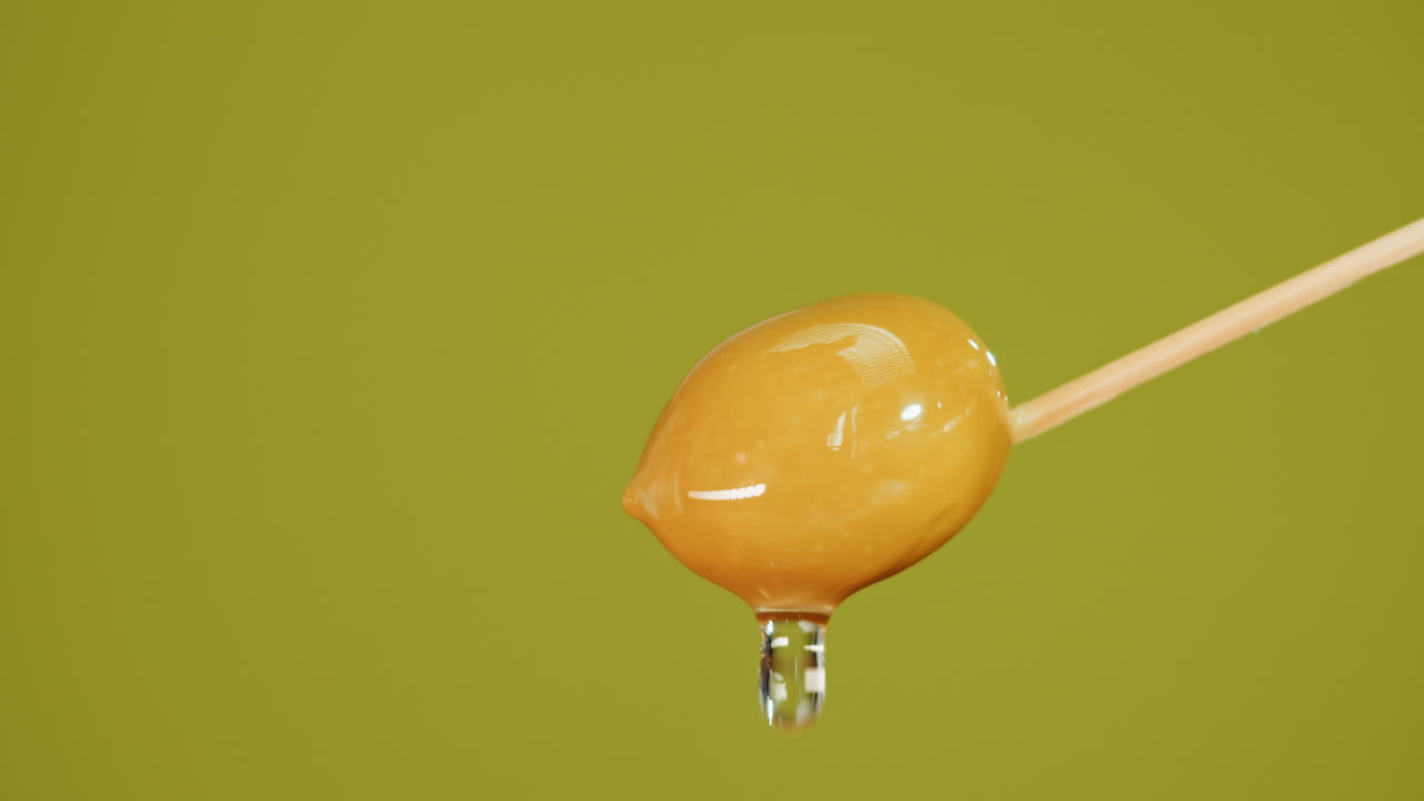 Closeup of a dripping olive on a wooden stick