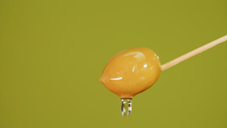 closeup of a dripping olive on a wooden stick