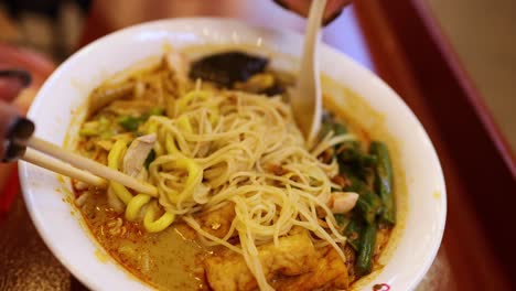 person enjoying noodle soup with chopsticks and spoon