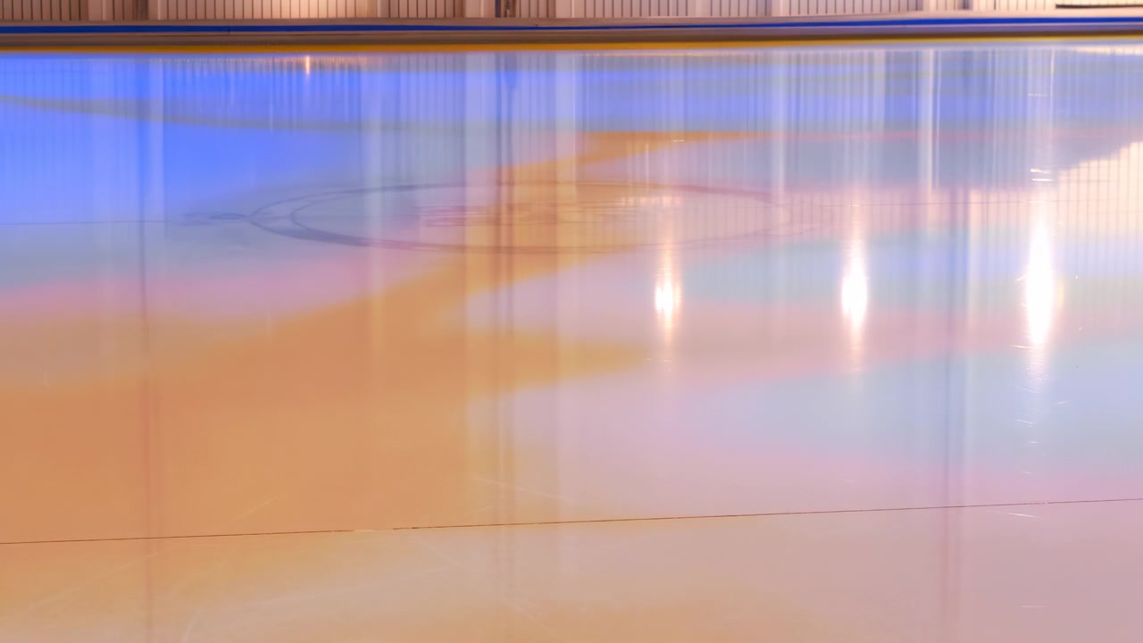 Panoramic low-eye-level view of indoor ice rink surface showing changing vertical light streaks, bright flares, glossy wet ice, faint circle marking, smooth lines and cool arena atmosphere