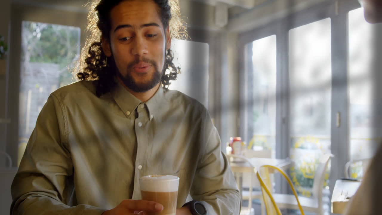 Mand med krøllet hår drikker kaffe på solbeskinnet café, afslappet atmosfære