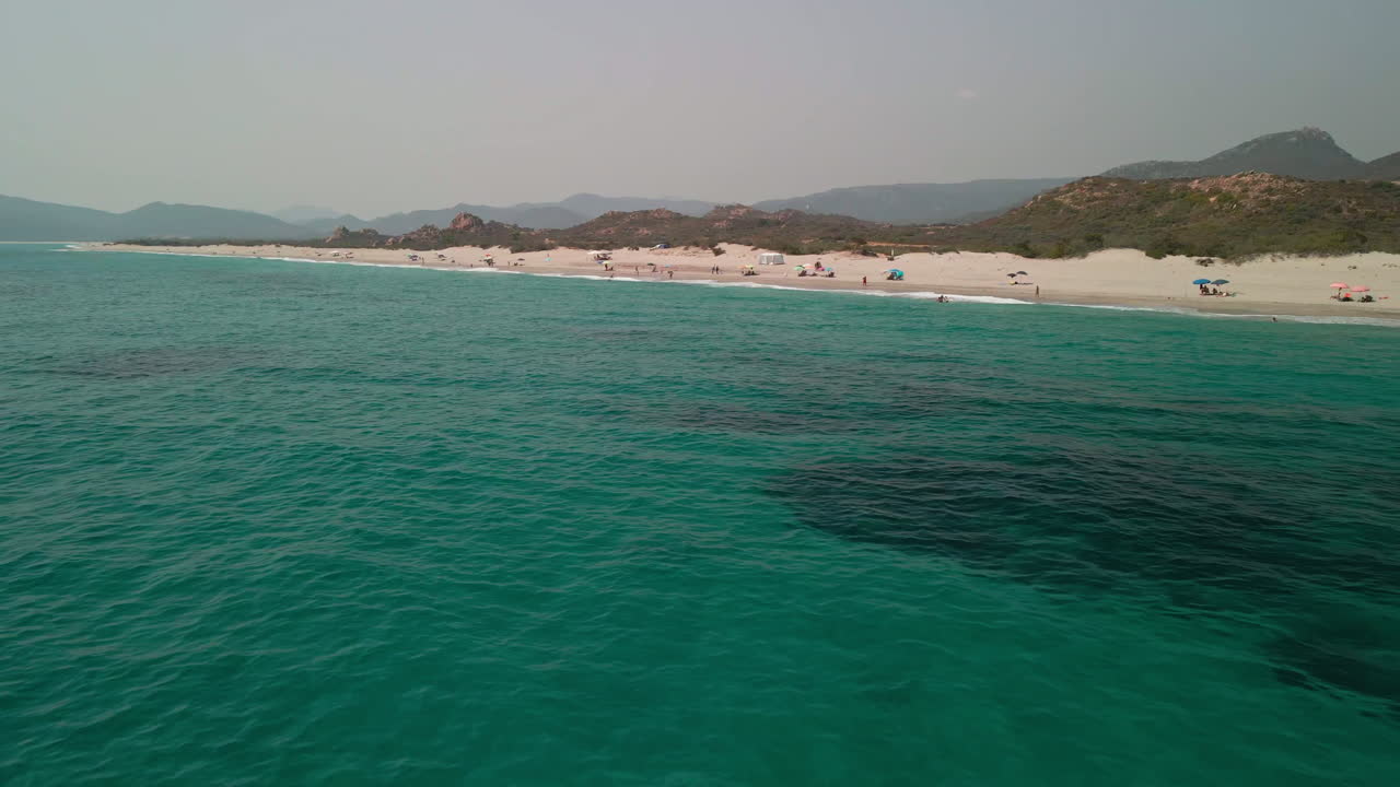 vista aérea de playa blanca con turistas y sombrillas coloridas durante el verano, montañas en el fondo en cerdeña, italia - disparo de drones