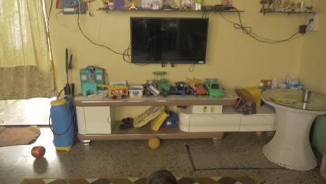 tiro inclinado que revela a un niño asiático, acostado en la alfombra, viendo la televisión solo en el pasillo y la unidad de televisión y el gabinete decorados con juguetes y trofeos