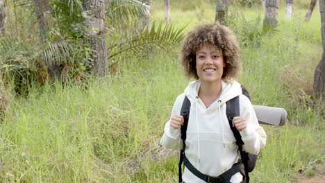 a young biracial woman with curly hair smiles while hiking, with copy space