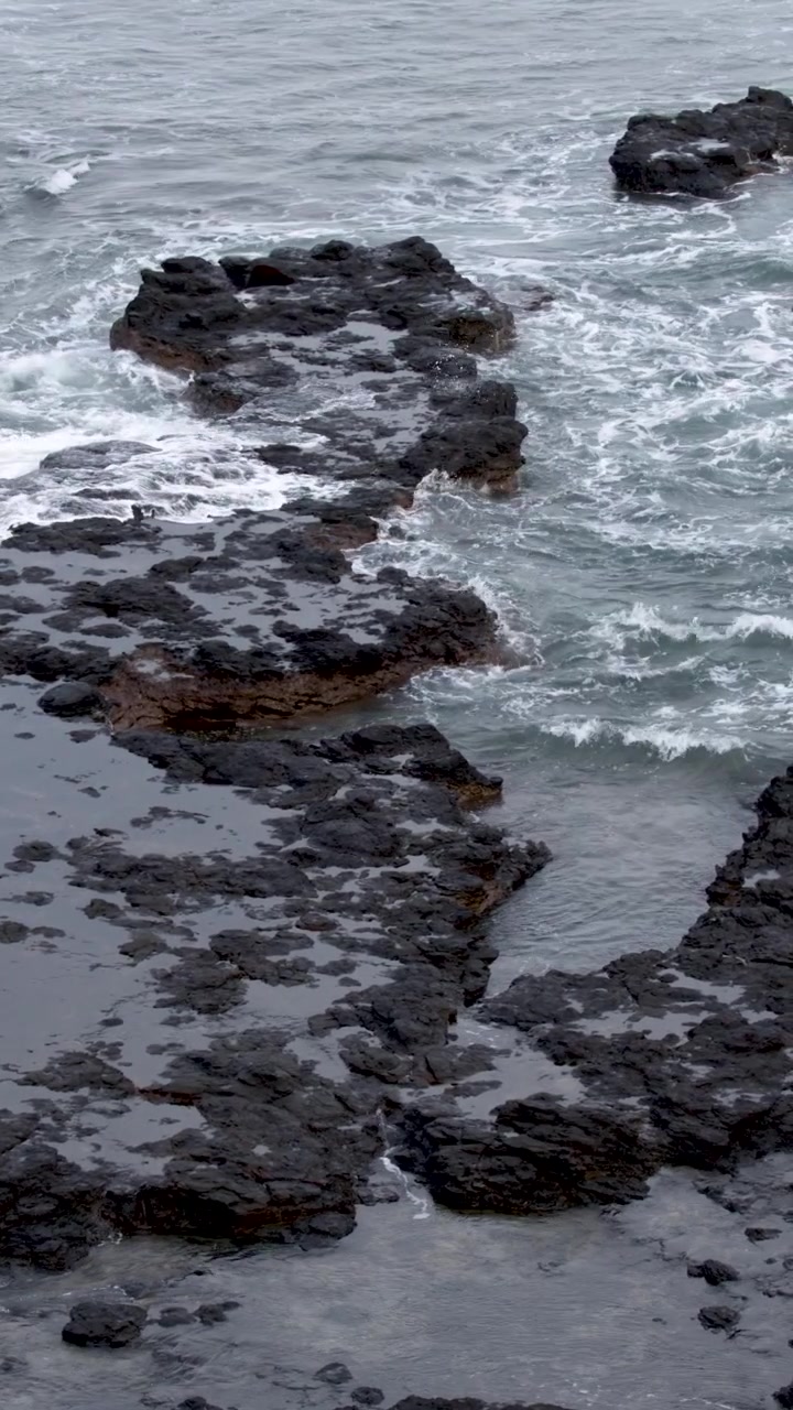 Vista dall'alto di schiuma bianca e onde che si infrangono su rocce vulcaniche scure in Australia