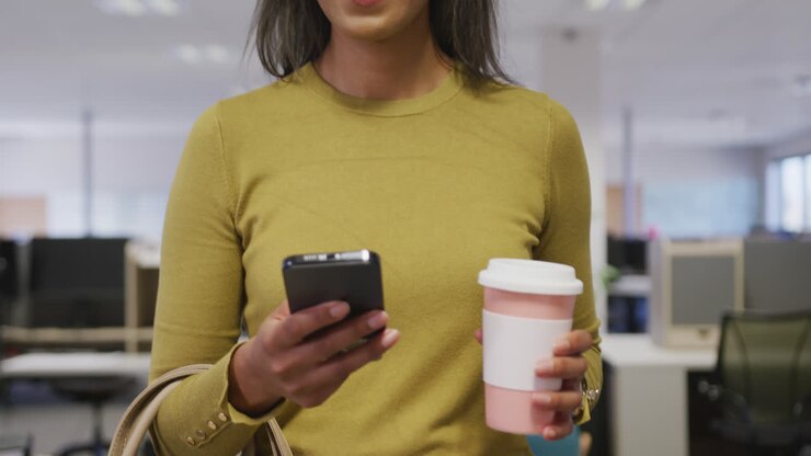 Biracial businesswoman smiling and walking with smartphone in office