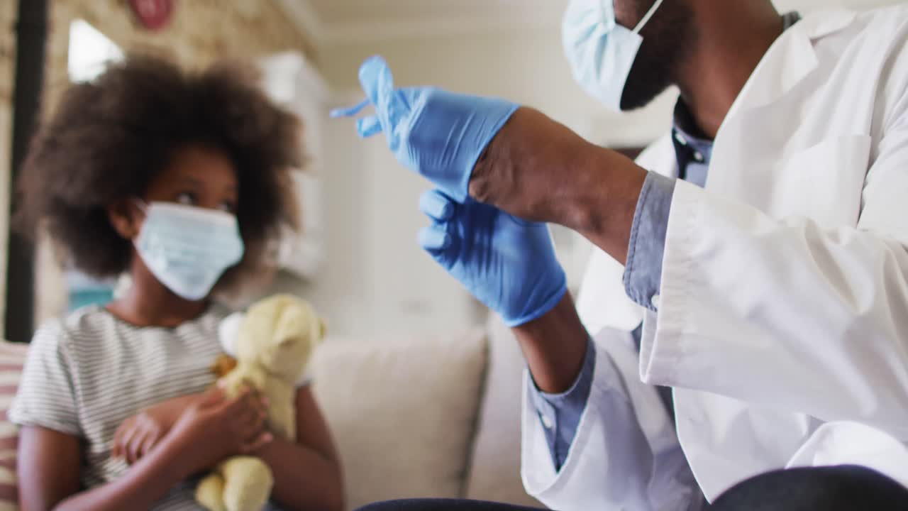 African american doctor in face mask wearing surgical gloves at home