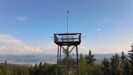 toma aérea de un dron volando hacia arriba e inclinándose hacia abajo mostrando la torre de observación pfannenstiel en el cantón de zúrich, suiza, revelando el lago en el fondo