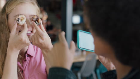 mujer rubia feliz posando con rosquillas amiga usando teléfono inteligente tomando fotos compartiendo diversión de fin de semana juntos en las redes sociales 4k