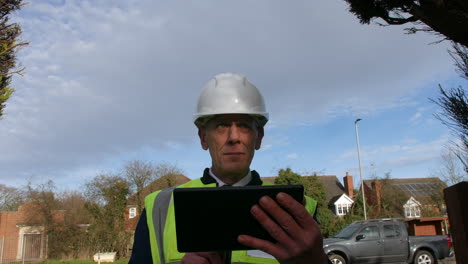 a happy senior architect examining plans of a large building on a tablet on a construction site in a residential street with traffic on the road in the background