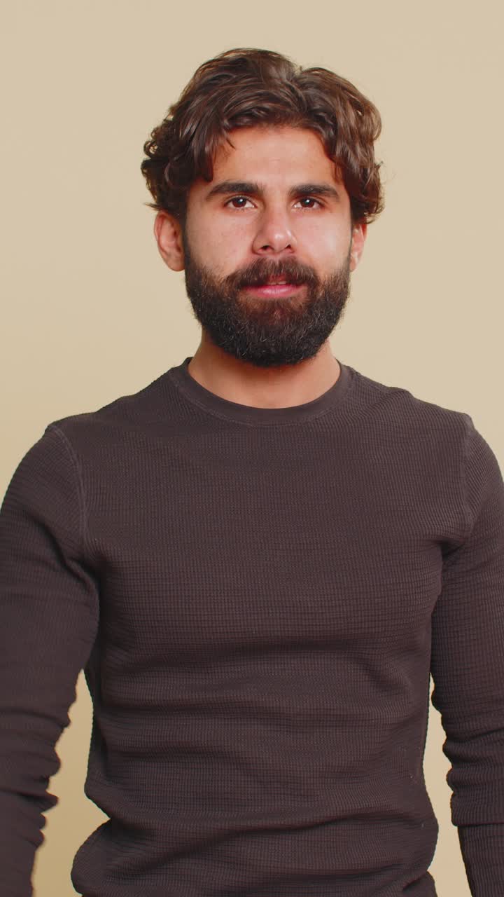 Indian young man pointing to camera and looking with playful happy expression on beige background