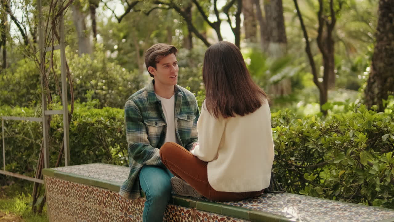 Happy young young pair man and woman laughing and talking sitting in park