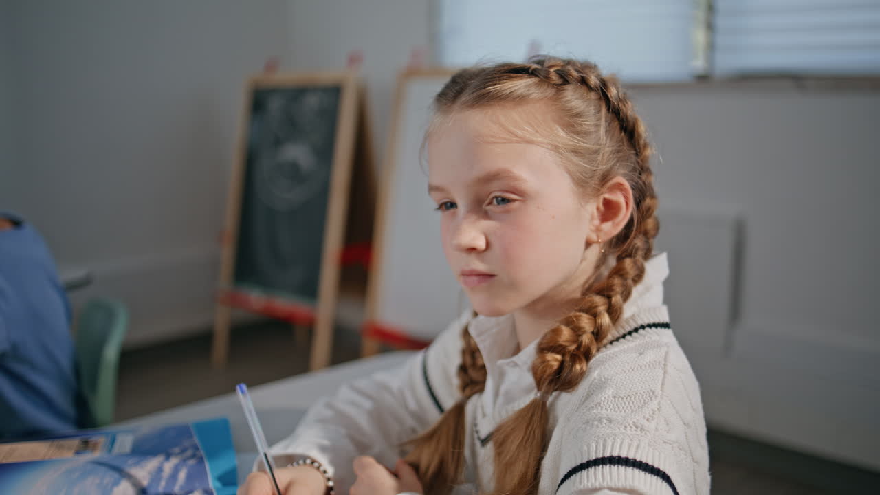 Thoughtful schoolgirl sitting desk closeup. Serious kid girl listening lesson