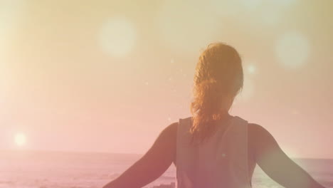 animation of light spots over biracial woman practicing yoga at beach