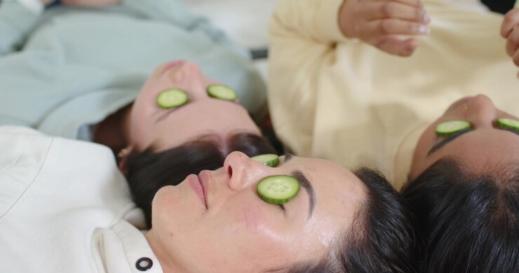 Diverse female friends relaxing on spa beds with attendant hands placing cucumber slices