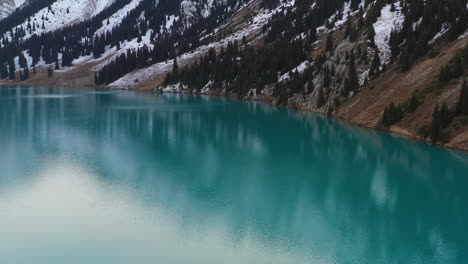 wide drone shot of the turquoise colored lake water at big almaty lake in the trans-ili alatau mountains in kazakhstan