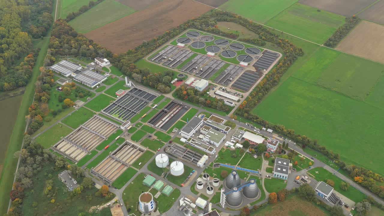 High angle perspective of a large sewage treatment facility surrounded by green fields. Industrial complex processing wastewater for purification