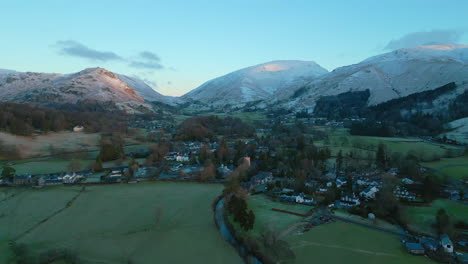 flying over english village at dawn towards sunrise lit snowy mountains at grasmere