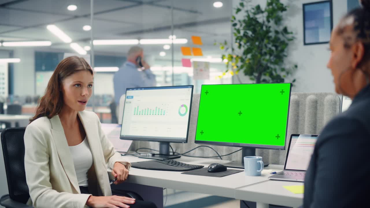 due colleghe parlano affettuosamente l'una con l'altra, ridono e sorridono mentre lavorano su computer con schermo verde in un moderno ufficio aziendale. manager e dipendente discutono di un progetto divertente.