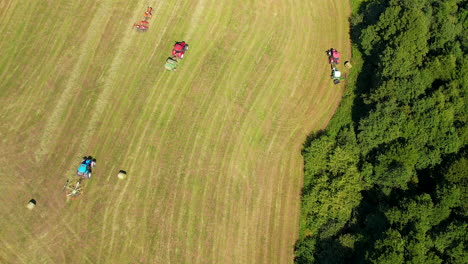aerial drone bird's eye view over tractors ploughing through large farmland on a bright sunny day