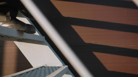 close-up leg of individual in black attire stepping down staircase in modern urban setting, with sunlight creating striking patterns and shadows on wall