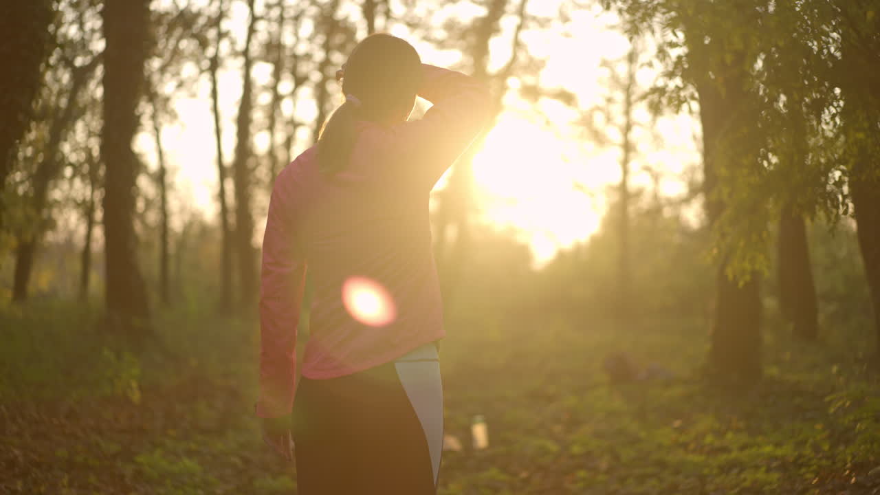 Woman exercising or resting in a sunlit forest at sunrise or sunset